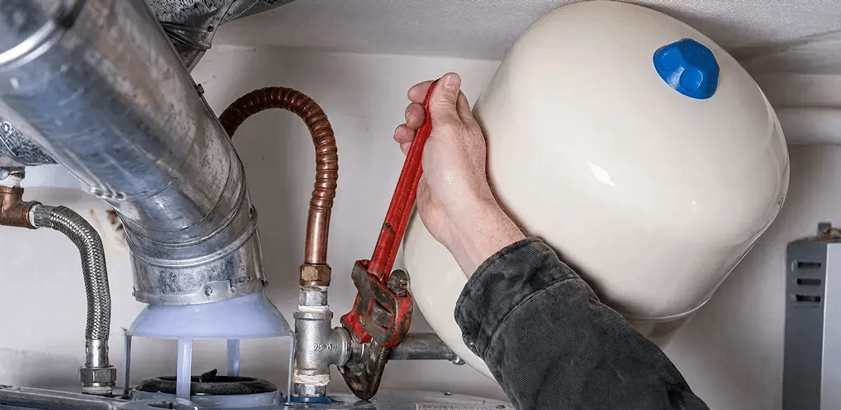 Water heater repair technician tightening plumbing connections near a tank unit in New Orleans, LA